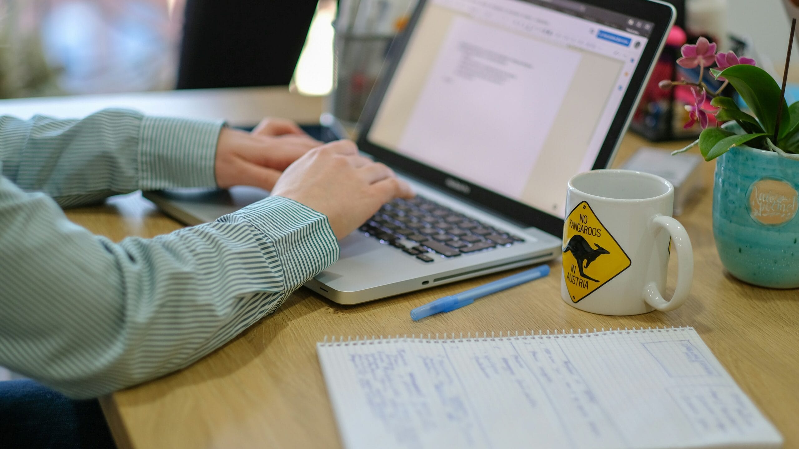 Blogger working on laptop using one of the best content AI tools with notes and coffee mug on desk