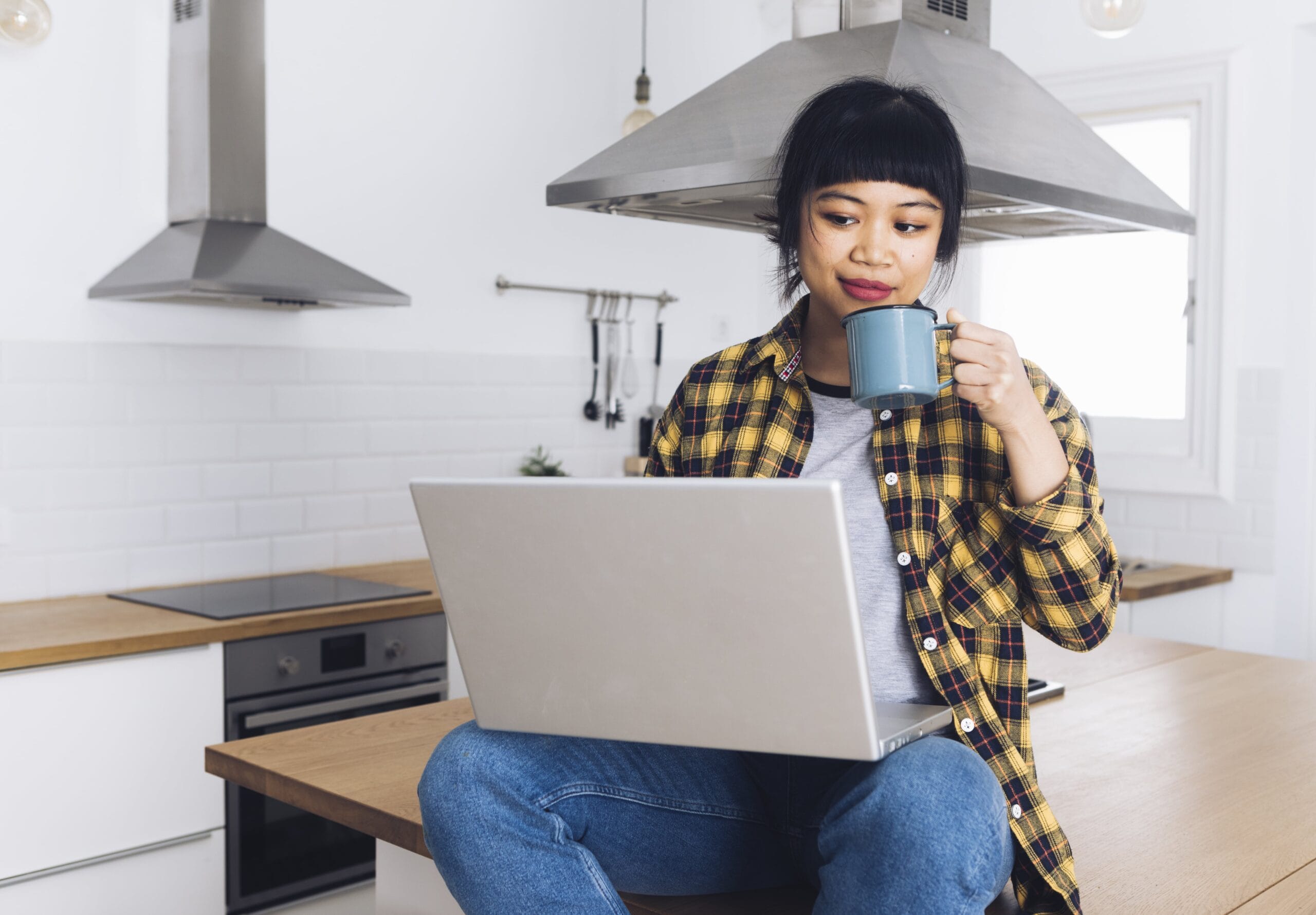 A young woman working on her laptop at home with a cup of coffee, representing beginners exploring AI jobs with no degree in a modern remote work setting.