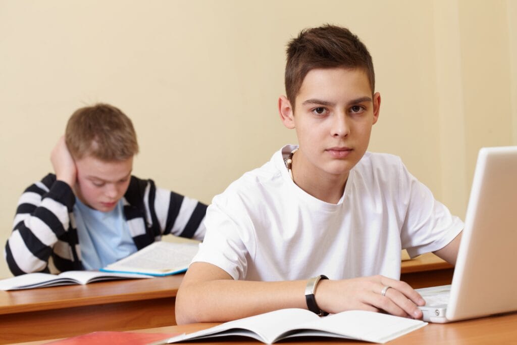 Teenage student using a laptop in a traditional classroom, contrasting formal education with the rise of AI jobs without a degree.